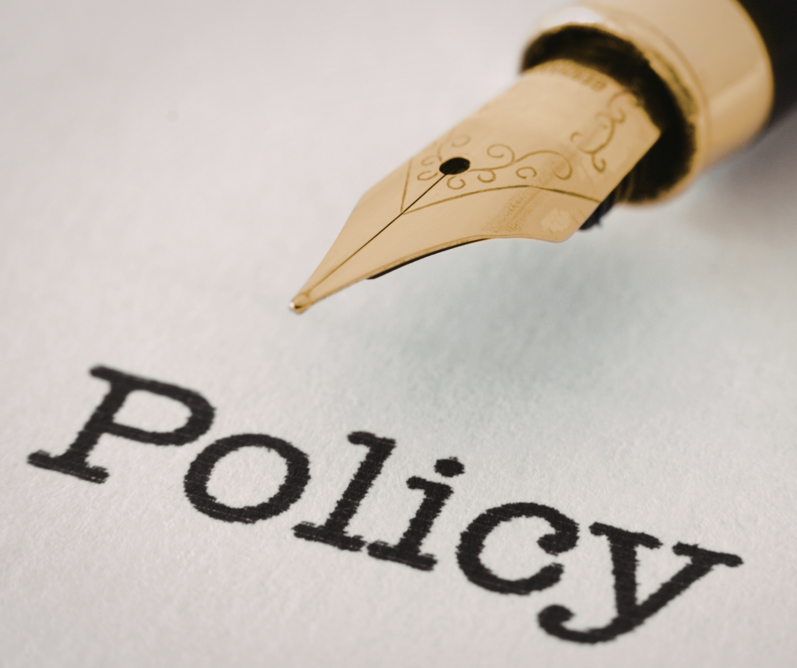 A close-up of a fountain pen tip poised above a sheet of paper with the word Policy printed in bold black letters.